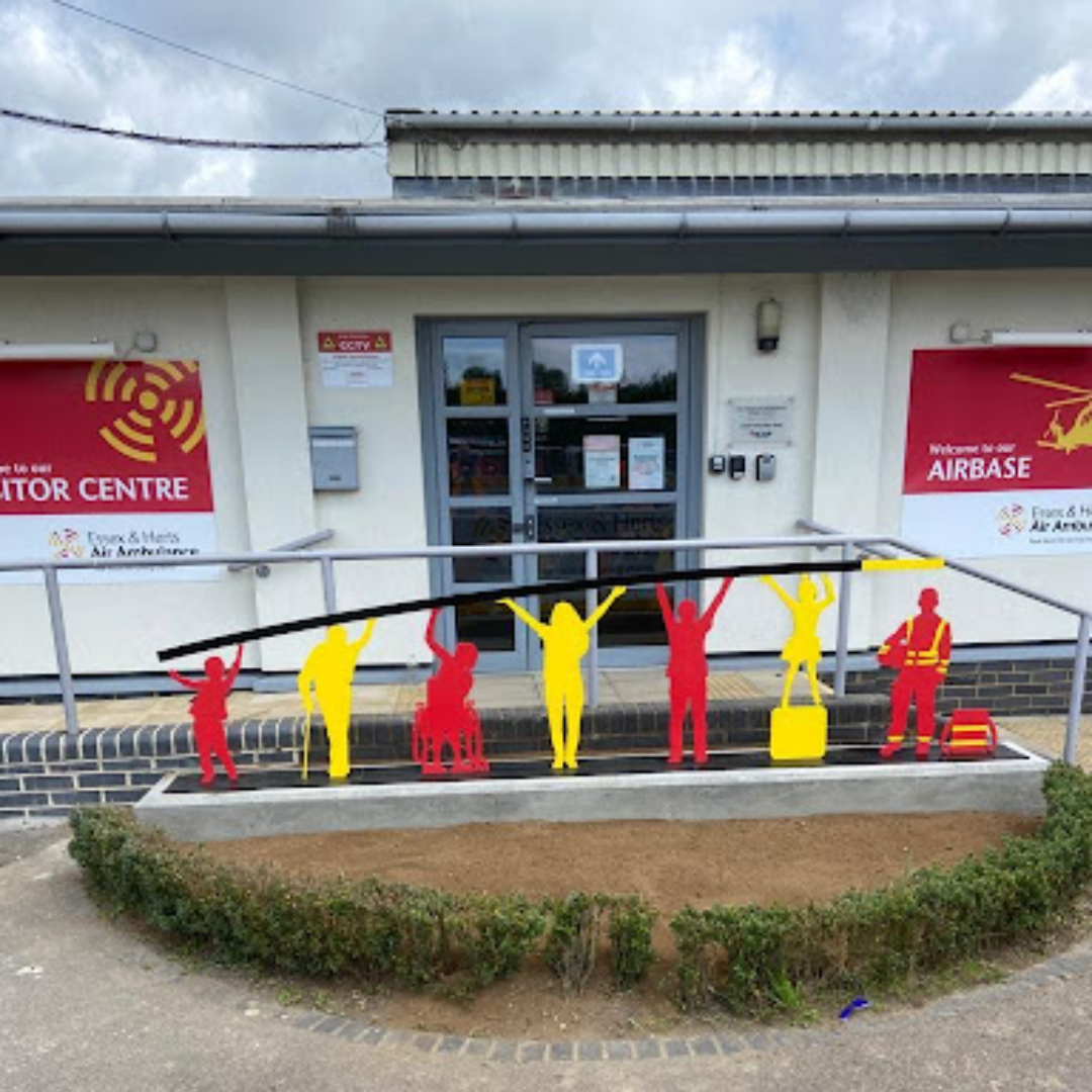 Custom fabricated bright yellow and red metalwork figures installed outside the Essex and Herts Air Ambulance visitor centre.