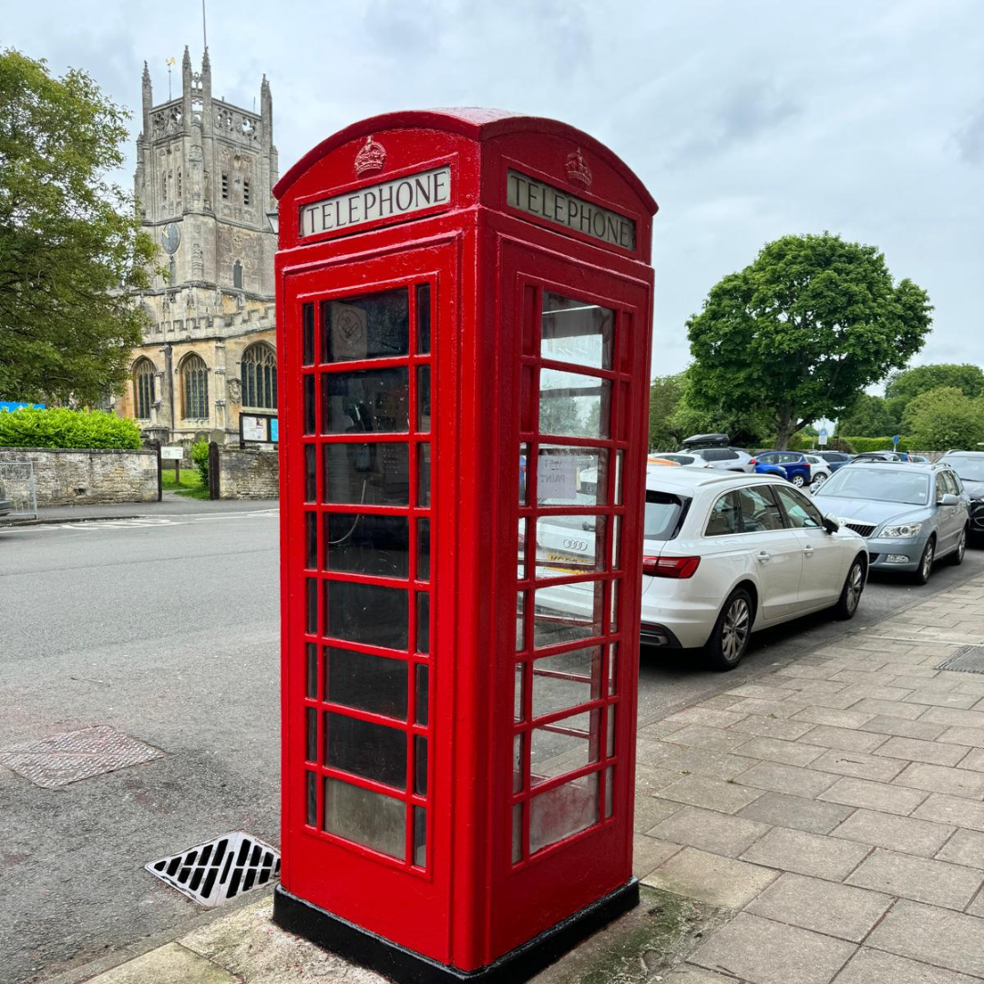 A meticulously restored classic red K6 telephone kiosk sitting on village grass.